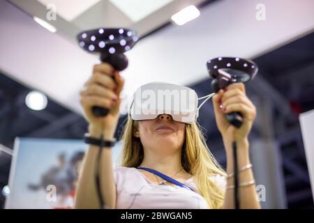 Junge kaukasische Mädchen in einem Virtual-Reality-Helm hält Kontrolle Sticks in den Händen und spielt ein Spiel. Font view, Soft-Focus, close up Stockfoto