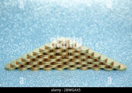Pyramide von Stapeln von Goldmünzen auf einem blauen Hintergrund. Stockfoto