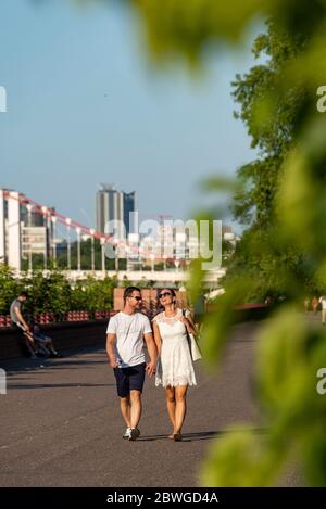 Ein trendiges junges Paar geht an einem warmen, sonnigen Sommertag auf dem themspfad im Battersea Park Chelsea London an den Händen Stockfoto