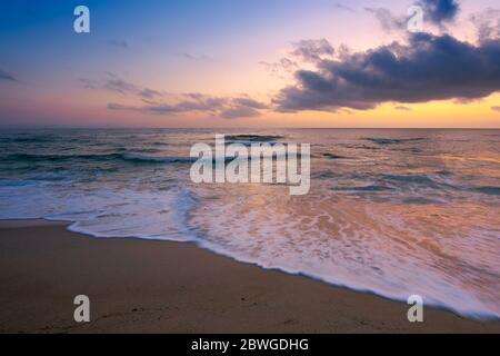 Meereslandschaft bei Sonnenuntergang. Schöne Landschaft von Sandstrand in lila Dämmerung. Welle läuft auf das Ufer. Wolken am Himmel über Horizont. Stockfoto