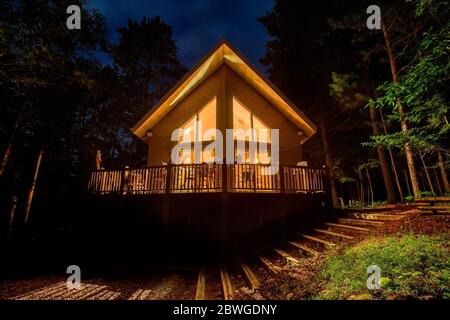 Ferienhaus mit beleuchteten Fenstern im Wald. Idyllische Hütte oder Hütte bei Nacht fotografiert. Konzepte können Reisen, Natur, Bogen, etc.. Umfassen Stockfoto