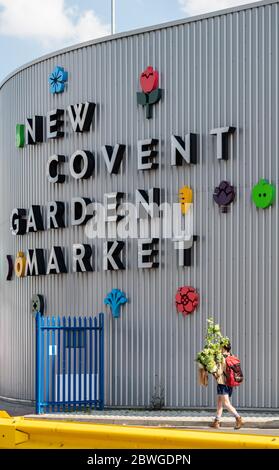 Eine Person, die Pflanzen trägt, spaziert vorbei an den farbenfrohen Schildern auf dem New Covent Garden Market in London, einem wichtigen Drehkreuz für den britischen Großhandel mit Blumen und Produkten. Stockfoto