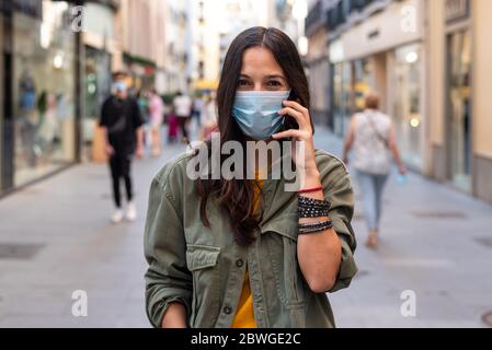 Frau, die auf der Straße ein Mobiltelefon benutzt und eine Schutzmaske im Gesicht trägt Stockfoto