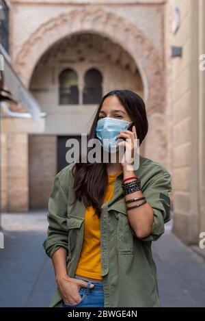 Frau, die auf der Straße ein Mobiltelefon benutzt und eine Schutzmaske im Gesicht trägt Stockfoto
