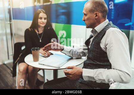 Zwei Kollegen aus der Wirtschaft unterhalten sich in einem Büro-Kaffeepunkt: Ein Mann Unternehmer im Vordergrund erklärt die Strategie-Nuance Stockfoto