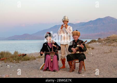 Kirgisische Musiker spielen traditionelle Instrumente. Mann in Weiß spielt Choor, Dame spielt Kyl Kiak, Mann sitzt spielt Komuz, in Issyik Kul, Kirgisistan Stockfoto