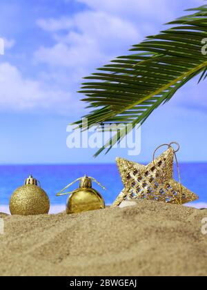 Weihnachtsferien Konzept. Weihnachtsschmuck auf einem Sandstrand mit Palmen, blauem Himmel und Meereshintergrund. Vertikales Foto Stockfoto