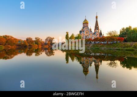 Spiegelbild einer russisch-orthodoxen Kirche in Almaty, Kasachstan, im Herbst bei Sonnenuntergang. Es ist bekannt als Kirche der Verherrlichung des heiligen Kreuzes. Stockfoto