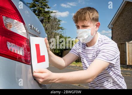 Teenager-Lernfahrer A trägt eine Gesichtsmaske wegen der Coronavirus-Pandemie warten, um seine Fahrstunde zu beginnen. Stockfoto