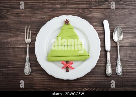 Serviette in Form eines Weihnachtsbaums mit Anisstern und Zimtstange als Baumstamm auf Teller, Draufsicht Stockfoto