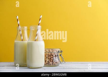 Zwei Flaschen vegetarische Sojamilch mit Soja im Glas auf gelbem Hintergrund Stockfoto