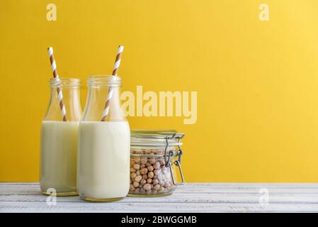 Zwei Flaschen vegetarische Sojamilch mit Soja im Glas auf gelbem Hintergrund Stockfoto