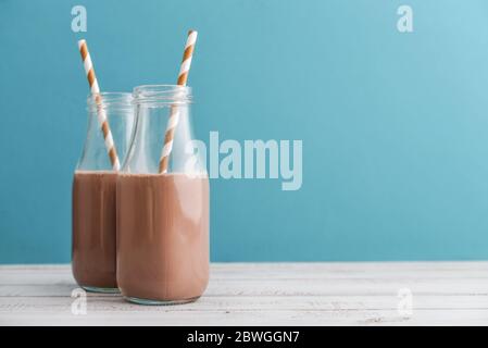 Zwei Flaschen Schokoladenmilch mit Trinkhalmen auf blauem Hintergrund Stockfoto