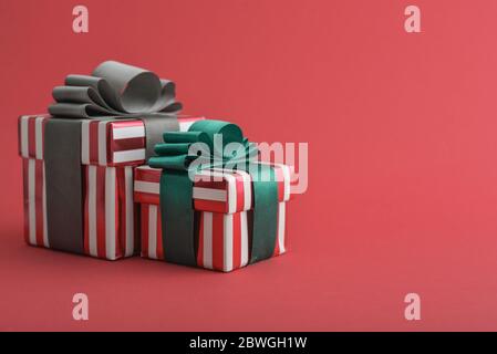 Zwei rot gestreifte Geschenkschachtel mit grünen und grauen Band auf rotem Hintergrund Nahaufnahme Stockfoto
