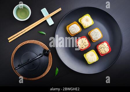 Mochi-Sortiment auf Teller mit Essstäbchen und grünem Tee - traditionelles japanisches Reisdessert, Draufsicht Stockfoto