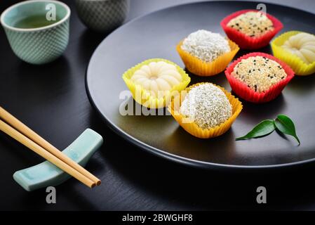 Mochi-Sortiment auf Teller mit Essstäbchen und grünem Tee - traditionelles japanisches Reisdessert, Nahaufnahme Stockfoto