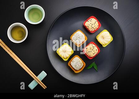 Mochi-Sortiment auf Teller mit Essstäbchen und grünem Tee - traditionelles japanisches Reisdessert, Draufsicht Stockfoto