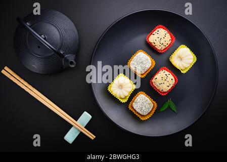 Mochi-Sortiment auf Teller mit Essstäbchen und grünem Tee - traditionelles japanisches Reisdessert, Draufsicht Stockfoto