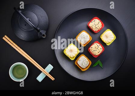 Mochi-Sortiment auf Teller mit Essstäbchen und grünem Tee - traditionelles japanisches Reisdessert, Draufsicht Stockfoto