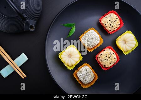 Mochi-Sortiment auf Teller mit Essstäbchen und grünem Tee - traditionelles japanisches Reisdessert, Draufsicht Stockfoto