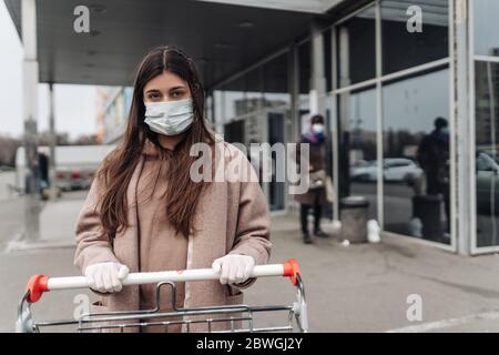 Junge Frau trägt Schutzmaske gegen Coronavirus 2019-nCoV und schiebt einen Einkaufswagen. Stockfoto