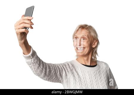 Freistil. Ältere Frau im Pullover stehend isoliert auf weiß Selfie auf Smartphone lächelnd fröhlich Stockfoto