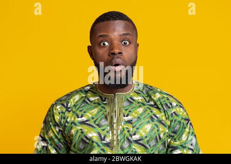 Betäubt afrikaner mit offenem Mund über gelbem Hintergrund Stockfoto