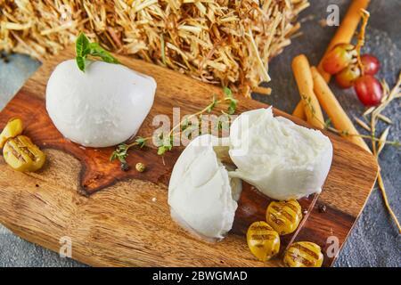 Fresca Mozzarella mit Knoblauch und geräucherten Oliven auf einem Holzständer auf grau-blauem Hintergrund. Italienischer Käse. Stockfoto