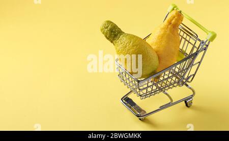 Lebensmittelwagen mit zwei hässlichen Zitronen auf hellgelben Hintergrund. Konzept Umwelt einkaufen, Bio-Lebensmittel, Copy space Stockfoto