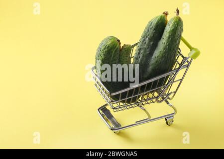 Lebensmittelwagen mit zwei hässlichen Gurken auf hellgelbem Hintergrund. Konzept Umwelt einkaufen, Bio-Lebensmittel, Copy space Stockfoto