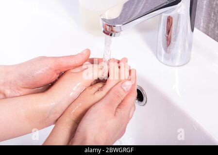 Mama wäscht die Hände ihres Babys unter fließendem Wasser in einem modernen Badezimmer Stockfoto