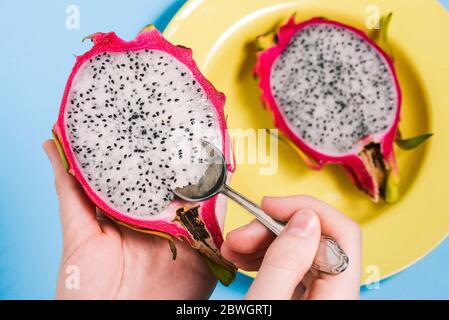 Eine Frau isst frische Pitaya mit einem Löffel. Schneiden Sie Pitaya Nahaufnahme in die Hände eines Mannes. Gesunde Ernährung. Ein veganes Gericht. Stockfoto