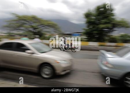 Caracas, Venezuela. Juni 2020. Zwei Leute auf einem Motorrad fahren an einer langen Schlange von Autos vorbei, die darauf warten, betankt zu werden. Angesichts der schweren Versorgungsprobleme mit Benzin und Diesel hat die venezolanische Regierung den Kraftstoffmarkt geöffnet und die Preise angehoben. Im Öl-reichsten Land der Welt war Benzin früher praktisch kostenlos, aber jetzt fehlt es Venezuela an Treibstoff. Zuletzt schickte der verbündete Iran mehrere Tanker mit Benzin nach Südamerika. Quelle: Rafael Hernandez/dpa/Alamy Live News Stockfoto