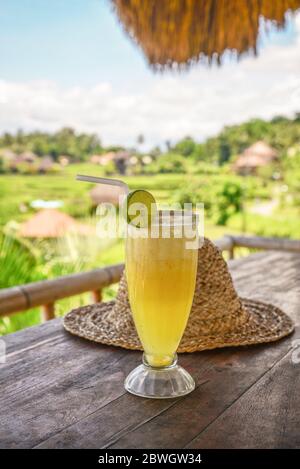 Ananassaft und Strohhut auf Holztisch im Café in der Nähe von Reis Terrasse an sonnigen Tag, Bali, Indonesien Stockfoto