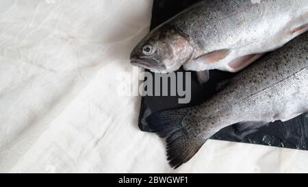 Zwei Regenbogenforellen auf einem schwarzen Steinbrett. Fisch für Suppe vorbereitet. Fisch Suppe Zutat. Ausschneiden der Fische Stockfoto