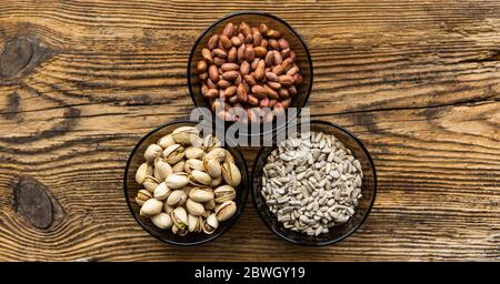 Sonnenblumenkerne, Pistazien und Erdnüsse in kleinen Tellern, die auf einem hölzernen Vintage-Tisch stehen. Nüsse sind ein gesundes vegetarisches Protein und Stockfoto