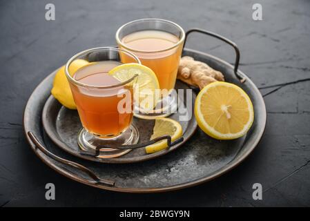 Hausgemachte fermentierte Rohkompucha Tee im Glas mit Zitrone und Ingwer auf schwarzem Hintergrund Stockfoto