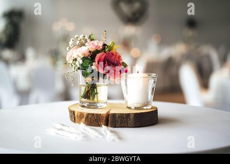 Elegante festliche Tischdekor mit bunten Blumen und Kerze auf Holzständer. Dekoration für Hochzeitstisch. Stockfoto
