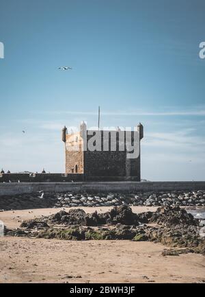 Sqala du Port, ein Verteidigungsturm am Fischerhafen von Essaouira, Marokko mit einer Schar von Möwen und blauem Himmel. Fischerboot im Vordergrund. Stockfoto