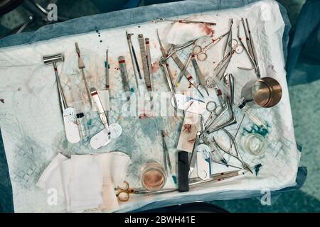 Chirurgische Instrumente und Instrumente, einschließlich Skalpellen, Pinzetten und Pinzetten, die während der Operation auf dem Operationstisch angeordnet sind. Stockfoto