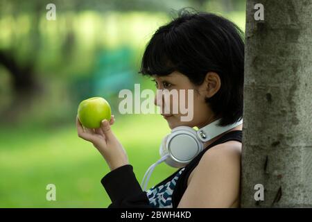 Gesunde asiatische Frau mit grünen Apfel im Garten. Lächelnde Menschen mit verschwommenem Hintergrund. Stockfoto