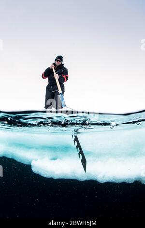 Expeditionsführer, mit einer speziellen, großen Handsäge, um die Eisscholle zu schneiden, so dass das Einstiegsloch unter dem Eisberg, Tasiilaq, Grönland, Nord-Atla zu tauchen Stockfoto