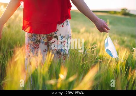 Nahaufnahme einer unerkennbaren Frau, die draußen ihre Maske wegwirft. Junge glückliche Mädchen Entfernen Schutzmaske. Ende des pandemischen Coronavirus-Konzepts. Wiesenlandschaft, Pollenallergie im Frühjahr. Stockfoto