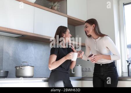 Zwei junge lachende Frauen stehen in der Küche und genießen Stockfoto