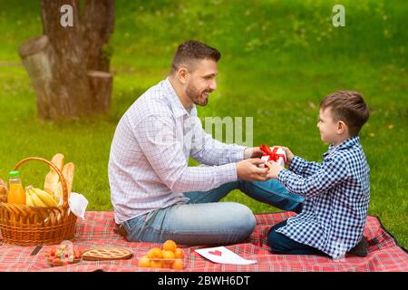 Feier zum Vatertag. Süße kleine Kind, die verpackte Weihnachtsgeschenk an seinen Papa auf Picknick im Freien Stockfoto