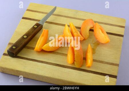 Frische rohe Aprikosenobstscheiben auf Holzschneidebrett mit Küchenmesser Stockfoto