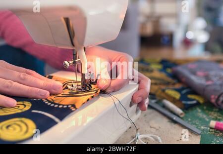 Eine Nahaufnahme einer Frau, die eine Nähmaschine benutzt, um ihre eigene Baumwollmaske zu machen. Stockfoto