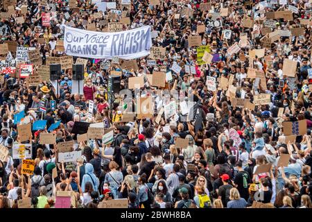 Tausende von Menschen versammelten sich auf dem Dam-Platz mit Protestplakaten und einem großen Banner mit der Aufschrift "Unsere Stimme gegen Rassismus" während des Protestes "Black Lives Matter" in Amsterdam.Tausende von Menschen nehmen an dem Protest "Black Lives Matter" am Dam-Platz in Amsterdam Teil, Um gegen die jüngste Tötung von George Floyd, einem schwarzen Mann zu protestieren, der in Polizeigewahrsam in Minneapolis, USA, starb, nachdem er von Minneapolis Polizeibeamten am Memorial Day zurückgehalten wurde. Stockfoto
