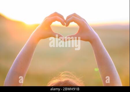 Hände machen Herzform mit Sonnenuntergang. Nahaufnahme der Frau Hände machen Herzform Geste. Qualitativ hochwertige Foto . Stockfoto