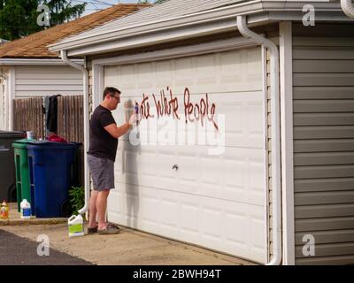 Oak Park Juni 2020. Ein Hausbesitzer reinigt rassistische Graffiti von seiner Garagentür. Die Graffiti erschien über Nacht auf der Nordseite dieses Chicagoer Vororts. Offensichtlich wussten die Purpetratoren, wer auf jedem getaggten Eigentum lebte, da sowohl anti-weiße als auch anti-schwarze Graffitti auf ausgewählten Eigenschaften verwendet wurde und mit dem Rennen der Hausbesitzer variierte. Stockfoto